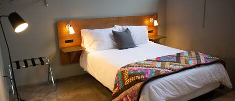 A neatly made bed with a colorful quilt, two bedside lamps, and a small bedside table.