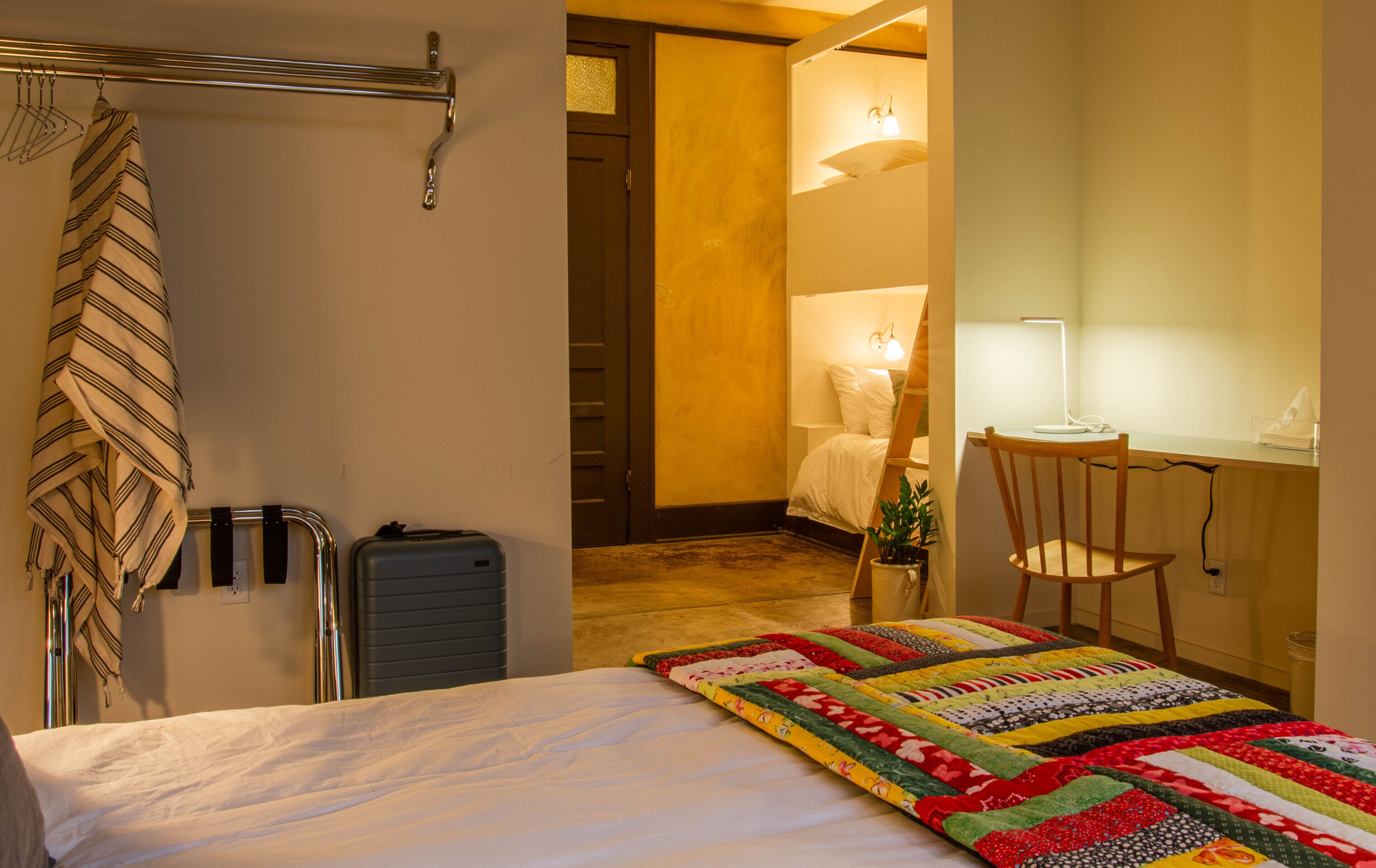 A hotel room with a bed, a desk with a chair, a suitcase, and a hanging towel.