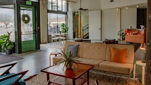 A spacious lobby with a green door, a beige sofa, a wooden coffee table, and a large window offering a view of the outside. - Travelers Hotel (Clarksdale)