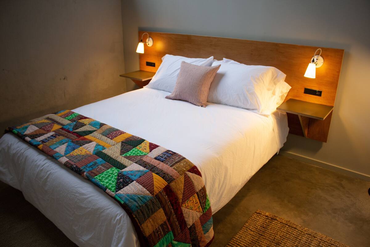 A neatly made bed with a quilt, two bedside lamps, and a nightstand.