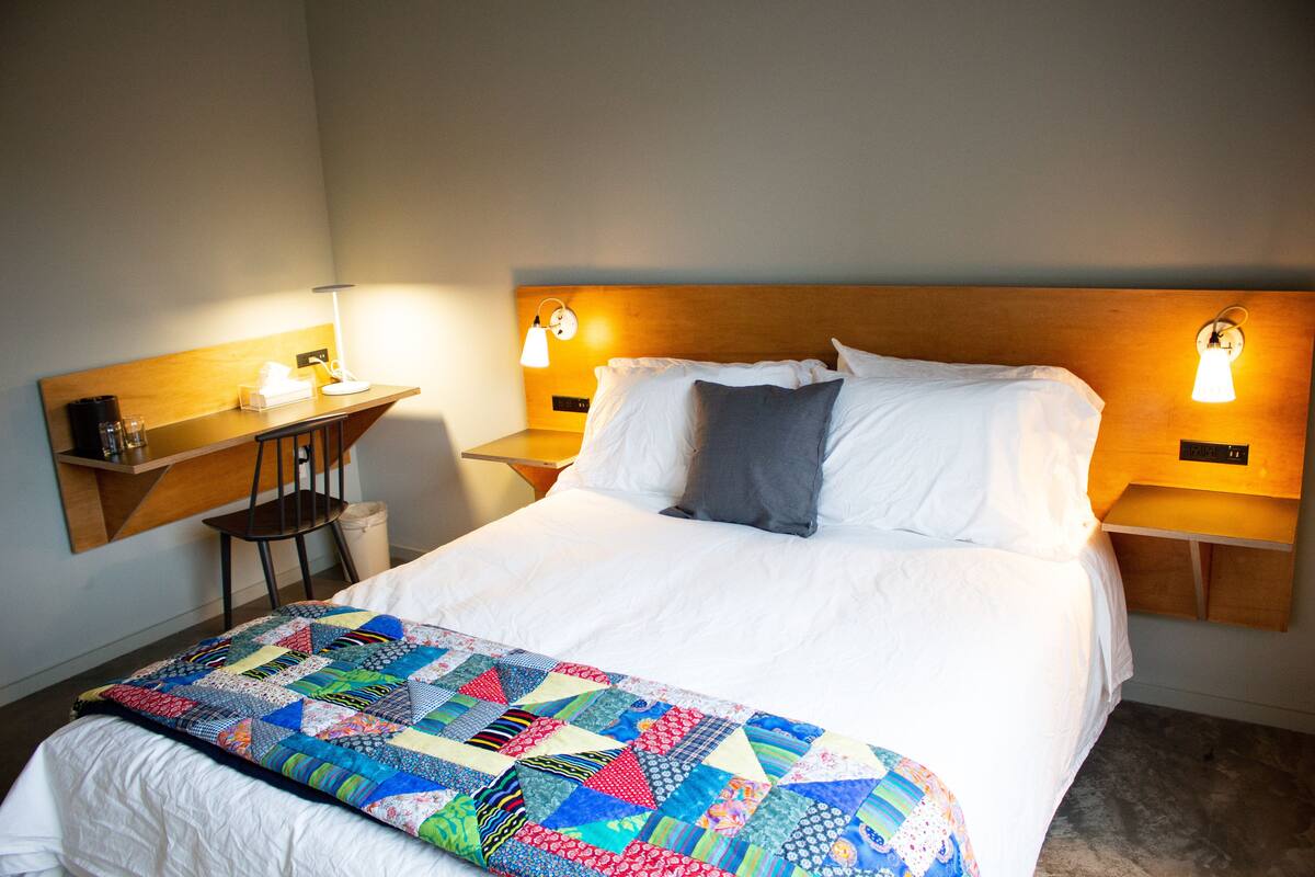 A neatly made bed with a colorful quilt, bedside tables with lamps, and a small desk with a chair.