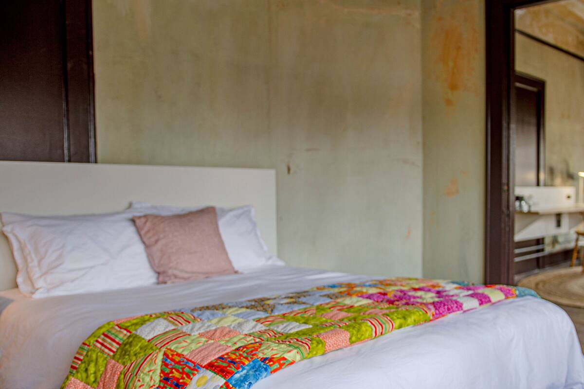 A bed with a colorful quilt, a white headboard, and a wooden door.