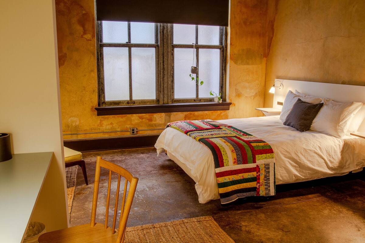 A bedroom with a bed, a chair, a desk, and a window with a view.
