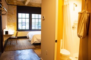 A room with a bed, a chair, a window, a toilet, and a shower area.