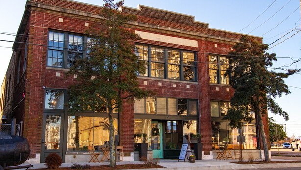 A two-story brick building with large windows and a green door, featuring outdoor seating and a signboard. - Travelers Hotel (Clarksdale)