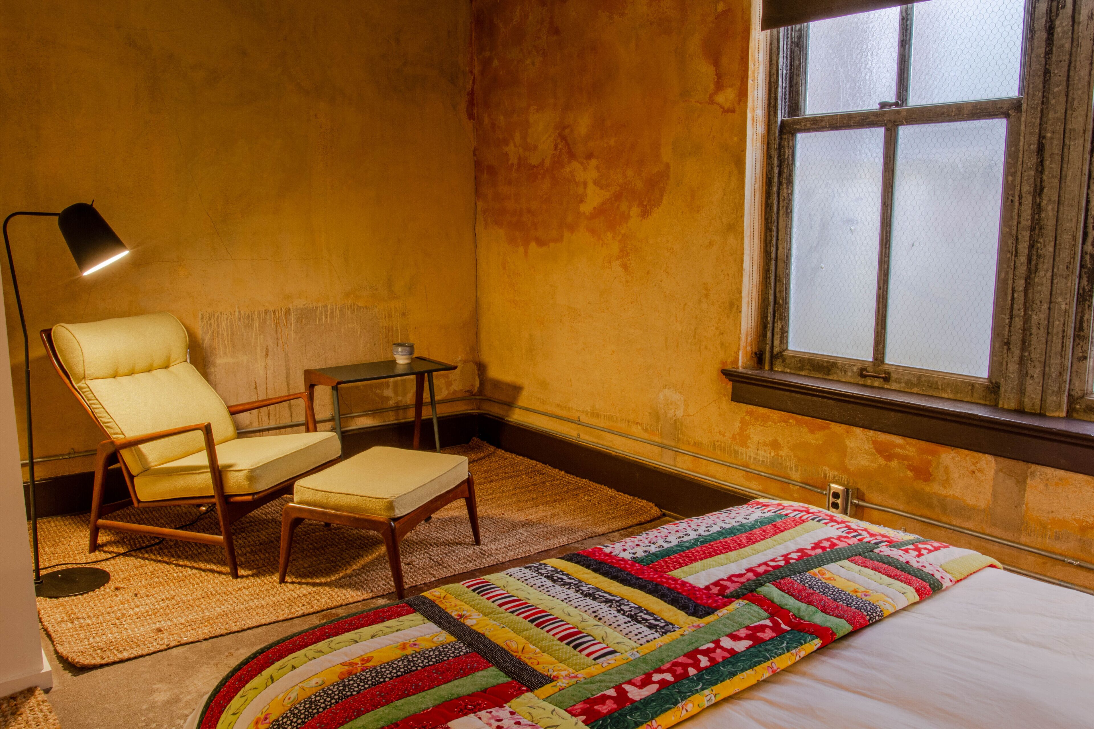 A room with a bed, a chair, a small table, a lamp, and a window.