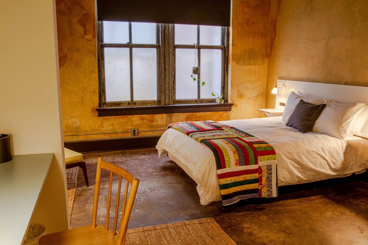 A bedroom with a bed, a chair, a desk, and a window.