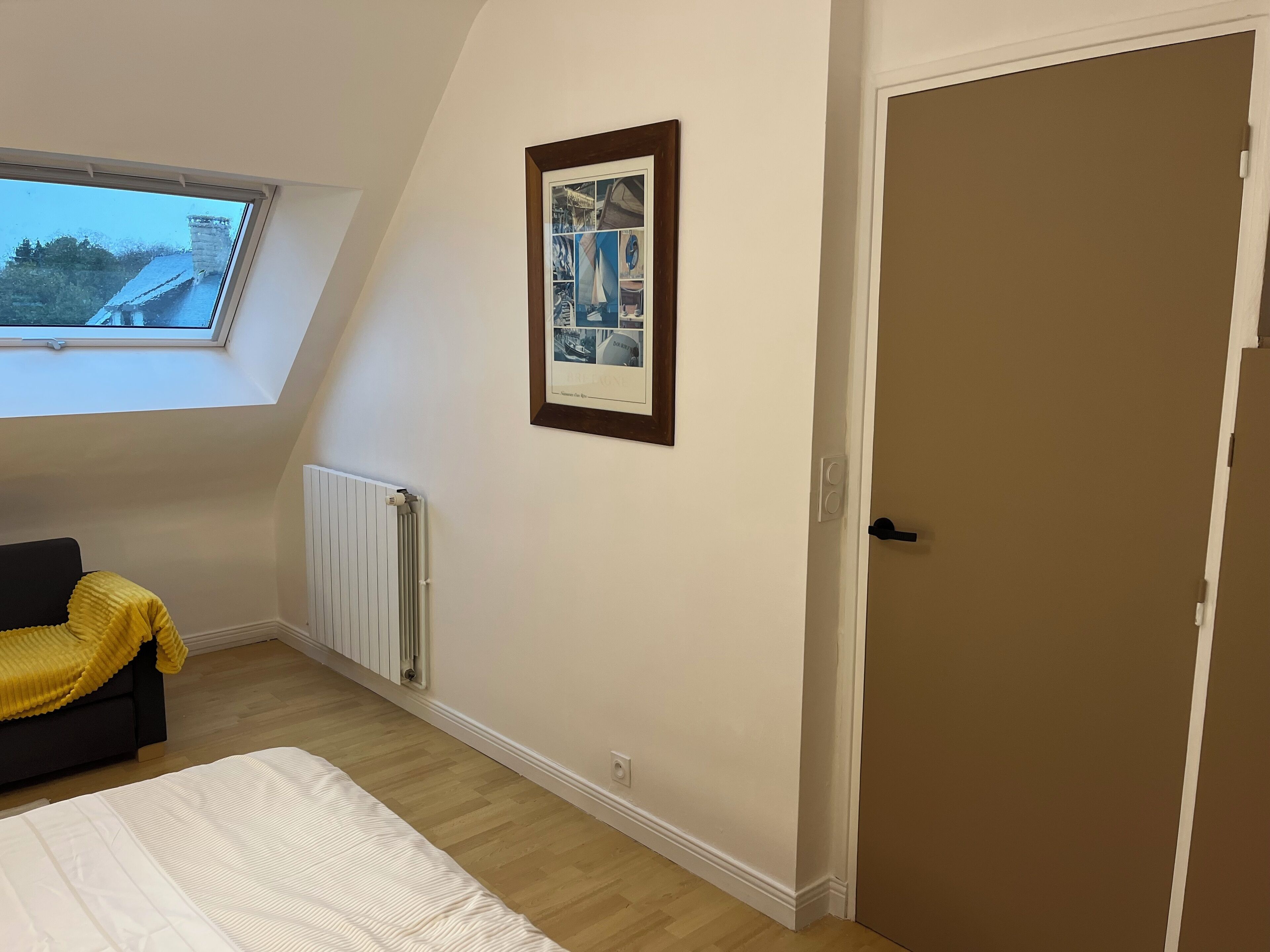 A bedroom with a bed, a radiator, a framed picture, a window, and a door.