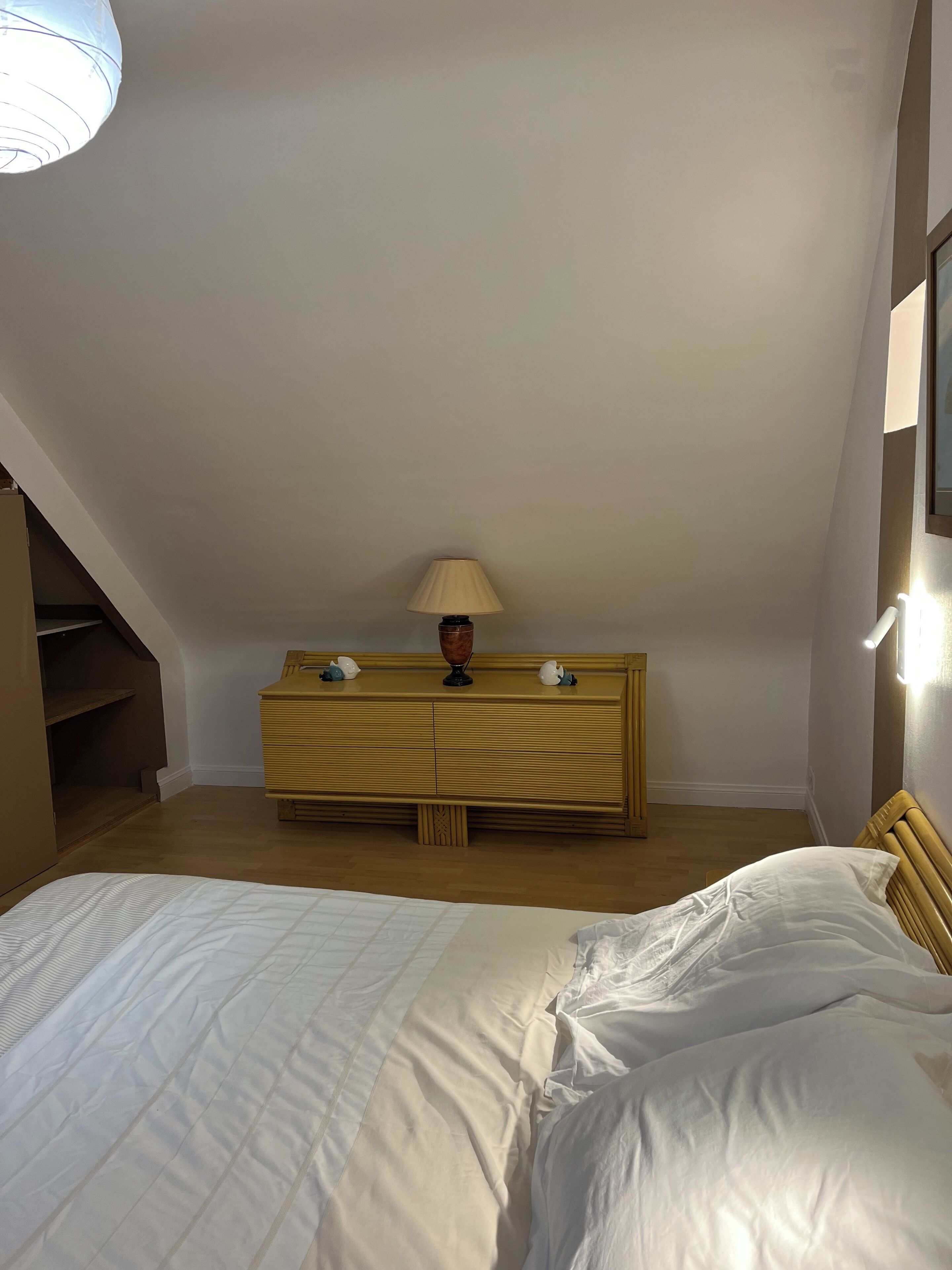 A bedroom with a bed, a wooden dresser, a lamp, and a staircase.