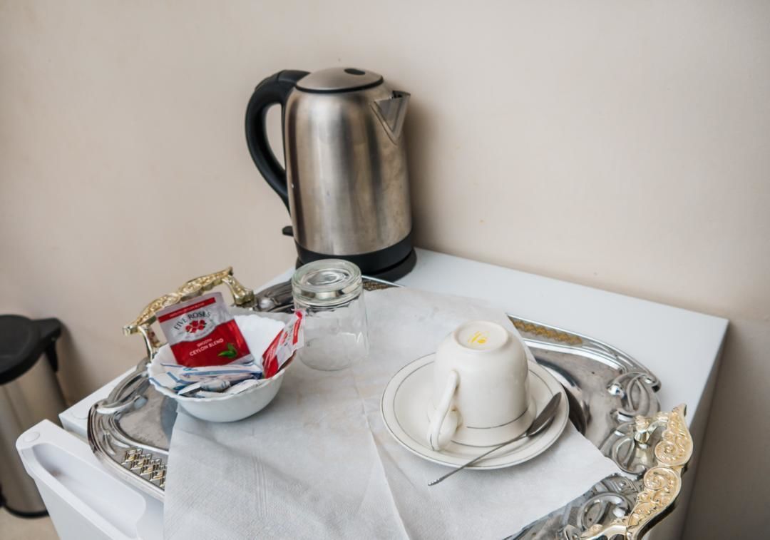 A neatly arranged breakfast setup with a kettle, teapot, cup, saucer, spoon, and a tray with a packet of tea and sugar.