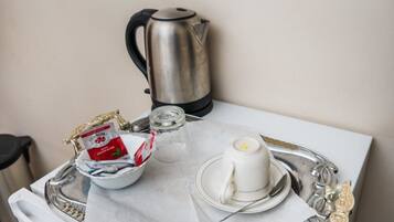 Una presentación ordenada para el desayuno con una tetera, un hervidor, una taza, un plato, una cuchara y una bandeja con una bolsita de té y azúcar.