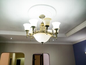 Un lustre à plusieurs bras et équipé de multiples points lumineux, dans une pièce dont le plafond et les murs sont de couleur unie.