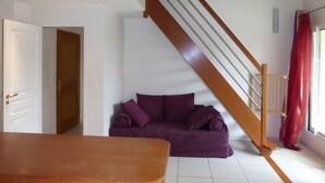 Una habitación con una escalera de madera, un sofá morado y una mesa de madera.