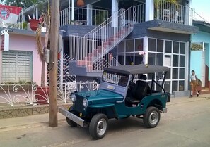 A teal jeep parked on a street in front of a building with a balcony and a sign that reads "FIESTA LOBSTER". - Hostal Merlyn TRINIDAD (Trinidad)