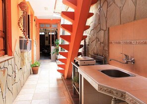 A narrow kitchen with a stone wall, a sink, and a staircase with orange railings. - Hostal Merlyn TRINIDAD (Trinidad)
