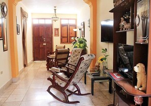 A living room with a wooden rocking chair, a sofa, a television, and a bookshelf. - Hostal Merlyn TRINIDAD (Trinidad)