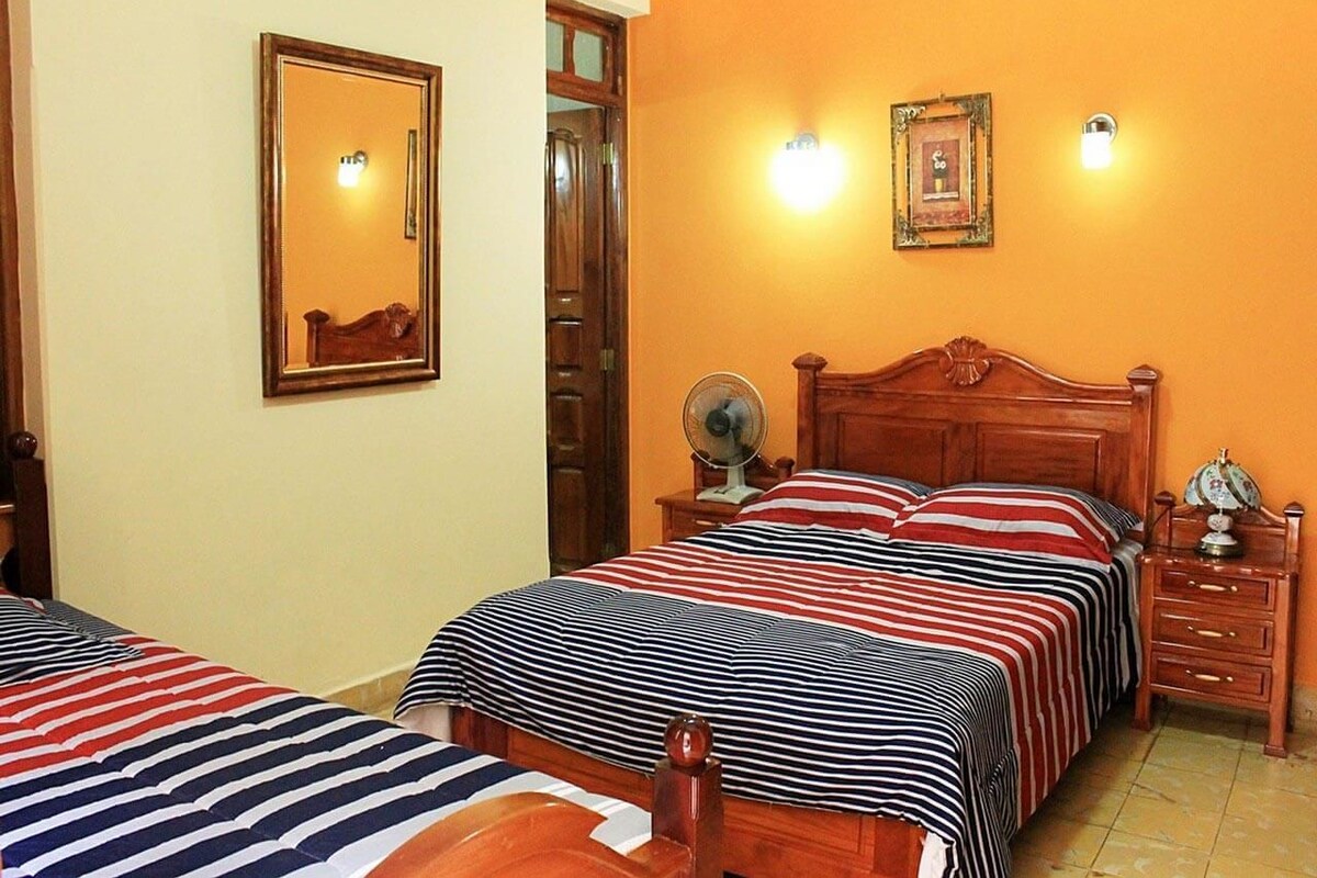 A hotel room with two beds, a wooden headboard, bedside tables, a mirror, and wall-mounted lights.