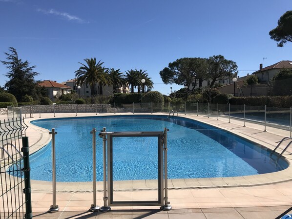 A swimming pool with a clear blue water, surrounded by a stone wall and metal railings.