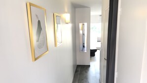 A hallway with a dark wooden floor, white walls, and framed artwork. There is a door on the right and a window at the end of the hallway. - Apartment renovated, air conditioning, sea view, swimming pools, tennis (Antibes)