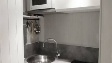 Une cuisine compacte dotée d’un évier en acier inoxydable, d’un four à micro-ondes et d’une plaque de cuisson intégrée.