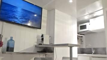 Une cuisine moderne équipée d’un téléviseur à écran plat, de meubles blancs, d’un bar en acier inoxydable et d’un four à micro-ondes.
