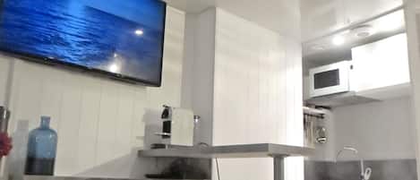 Una cocina moderna con un televisor de pantalla plana, armarios blancos, una barra de acero inoxidable y un microondas.