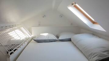 Una piccola camera da letto bianca con un letto singolo, un soffitto spiovente e un lucernario.