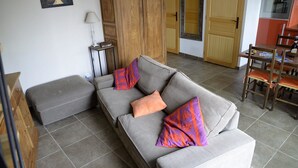 Un salón con un sofá gris, almohadas naranjas y moradas, una mesita con lámpara y un armario de madera.