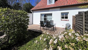 Una casa blanca con techo de tejas rojas, una terraza de madera y un jardín con flores.