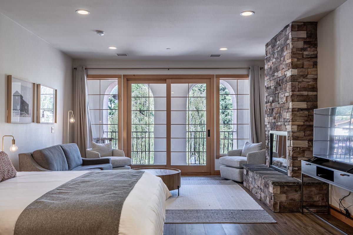 A modern bedroom with a large bed, two seating areas, a stone fireplace, and a television.