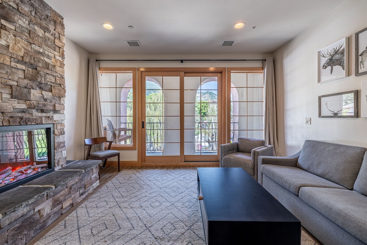 A living room with a stone fireplace, a sofa, a coffee table, and a view through large glass doors.