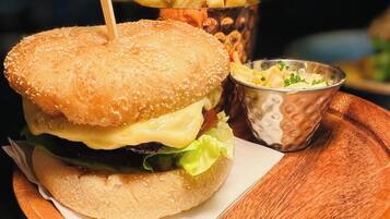 Hamburguesa con pan de sésamo, queso, lechuga y un palillo, acompañada de papas fritas y un bol pequeño de ensalada de col.