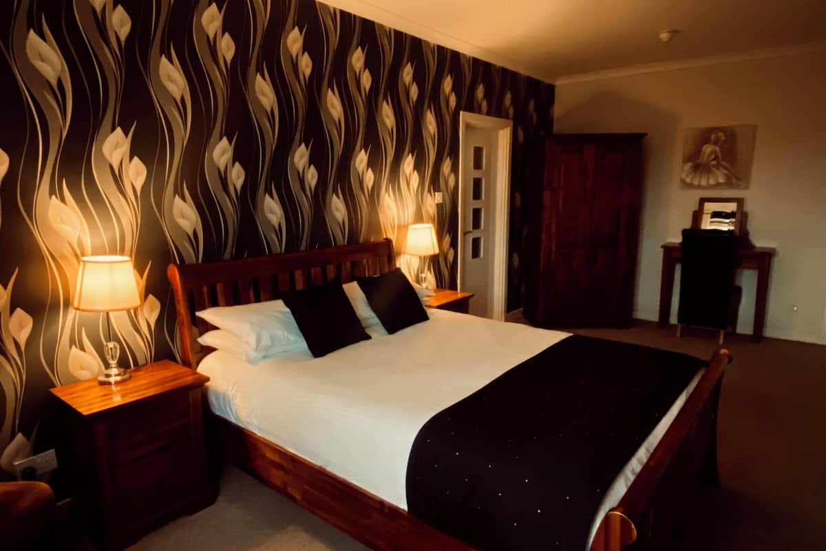 A neatly made bed with a black and white patterned headboard, two bedside lamps, and a wooden nightstand.