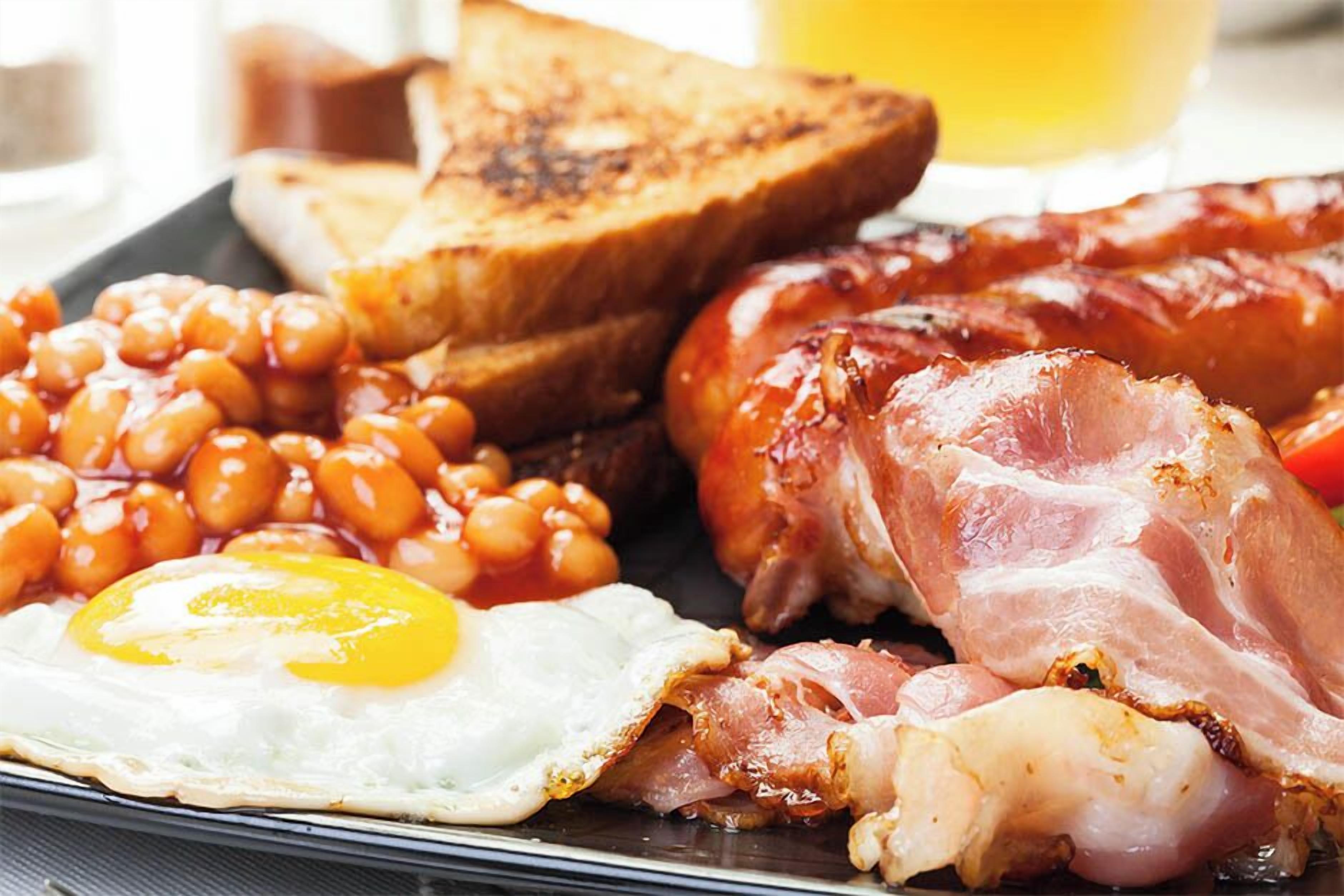 A breakfast plate with eggs, bacon, beans, toast, and sausages.