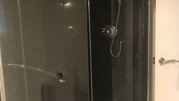 A glass-enclosed shower stall with a white door, a towel hanging on a rack, and a showerhead.