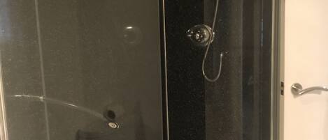 A glass-enclosed shower stall with a white door, a towel hanging on a rack, and a showerhead.