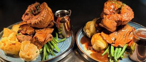 Two plates of food with meat and vegetables, accompanied by a small metal pitcher.