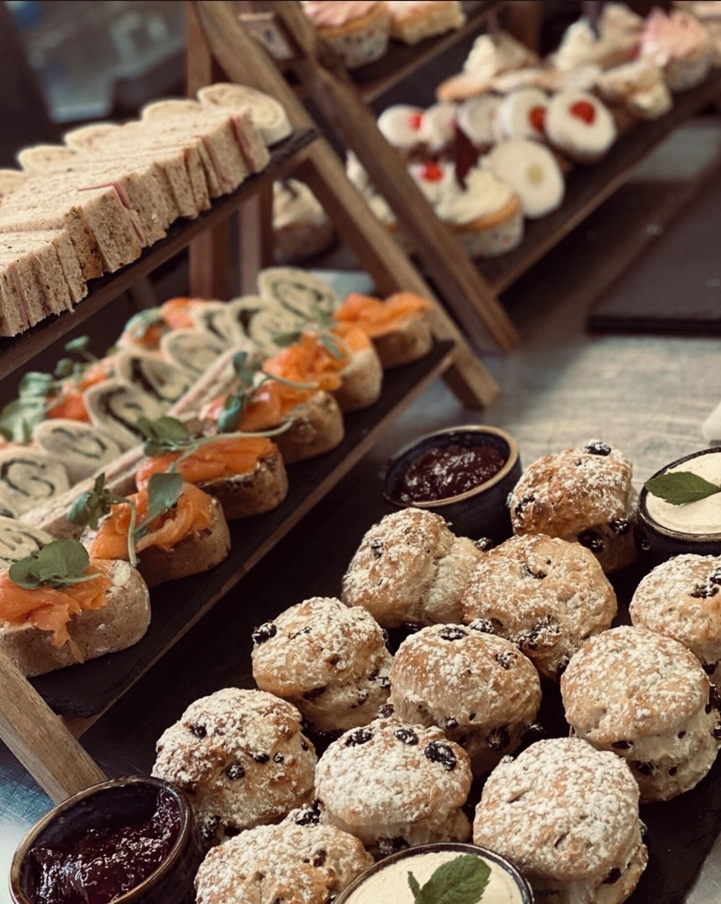 A variety of pastries and desserts on display, including scones, sandwiches, and pastries with various toppings and fillings.