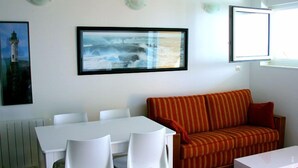 Ett rum med ett vitt bord och stolar, en randig orange soffa och två inramade tavlor på väggen.