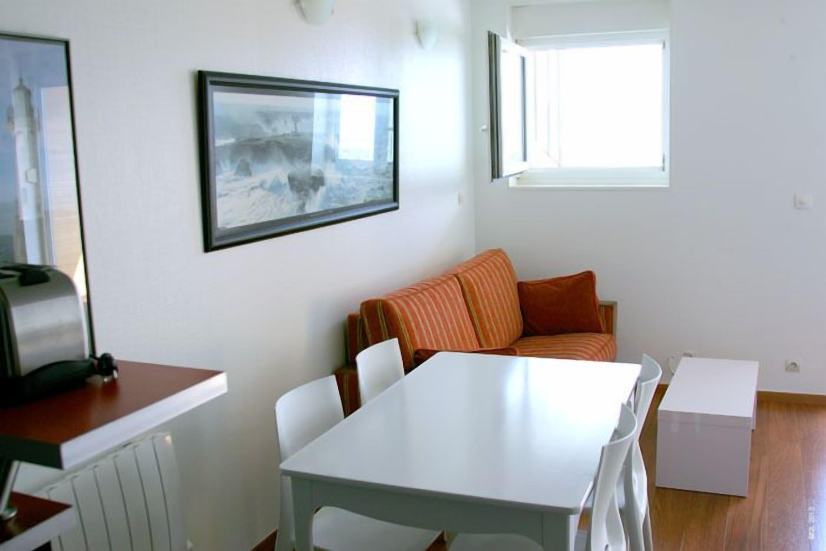 A room with a white table and chairs, a striped orange sofa, and a framed picture on the wall.