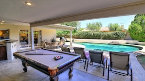 A pool table with chairs and a bar area, a pool, and a covered patio.