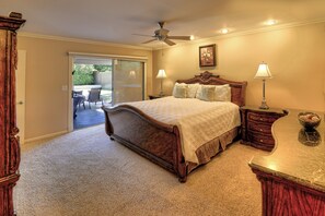 A bedroom with a bed, two bedside tables, a nightstand, a ceiling fan, and a view through a sliding glass door to an outdoor patio.