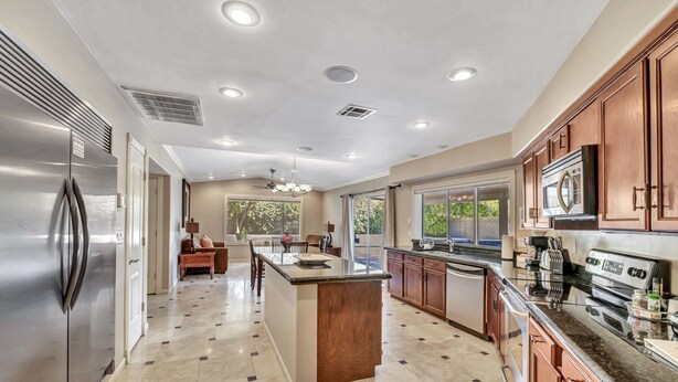 A spacious kitchen with a central island, stainless steel appliances, wooden cabinets, and a large window providing natural light.