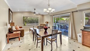 A dining area with a wooden table, chairs, a chandelier, and a large window.