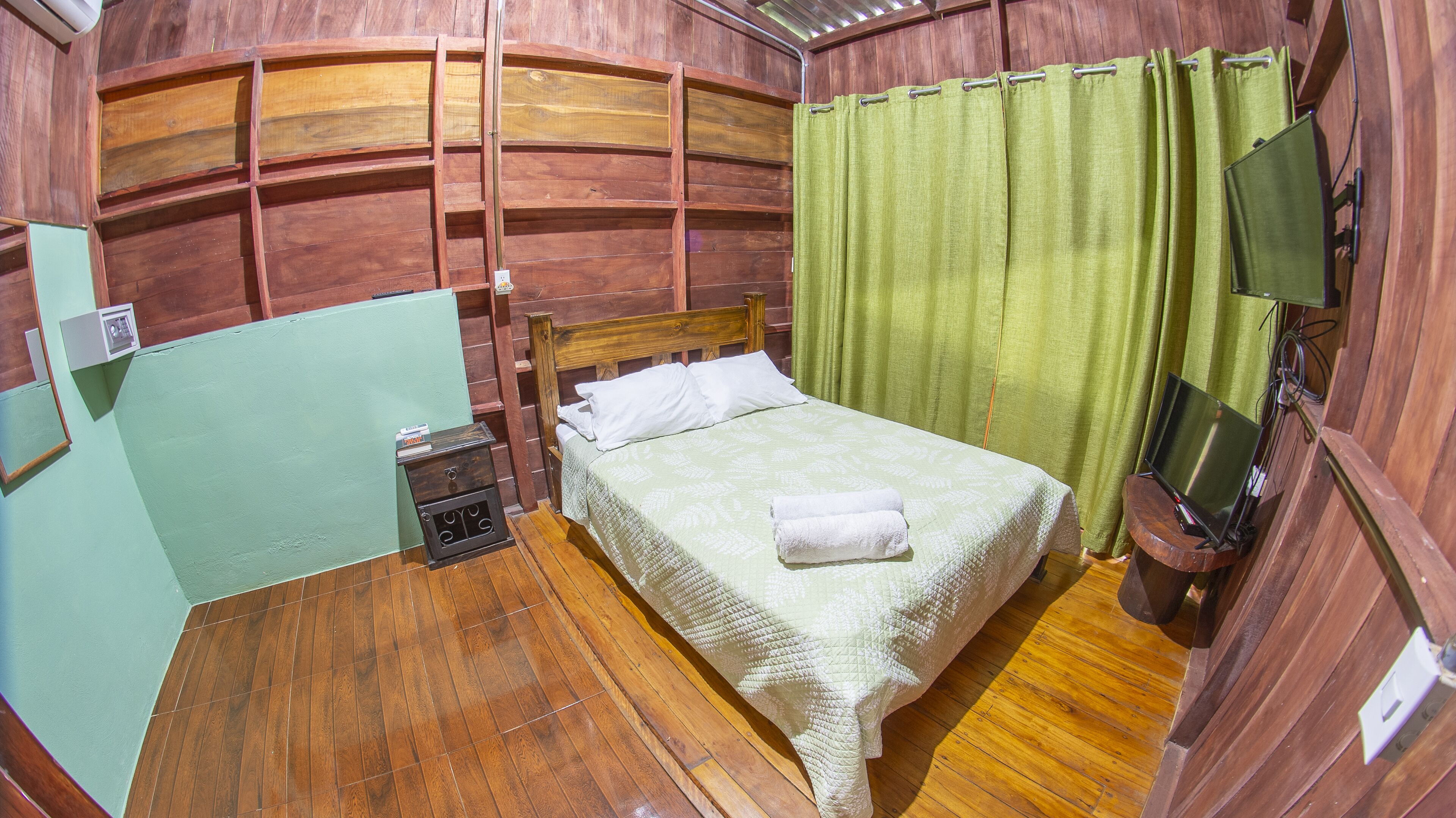 Une pièce en bois avec un lit, une table de chevet, un téléviseur et un rideau vert.