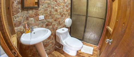 A bathroom with a stone wall, a sink, a toilet, and a shower.