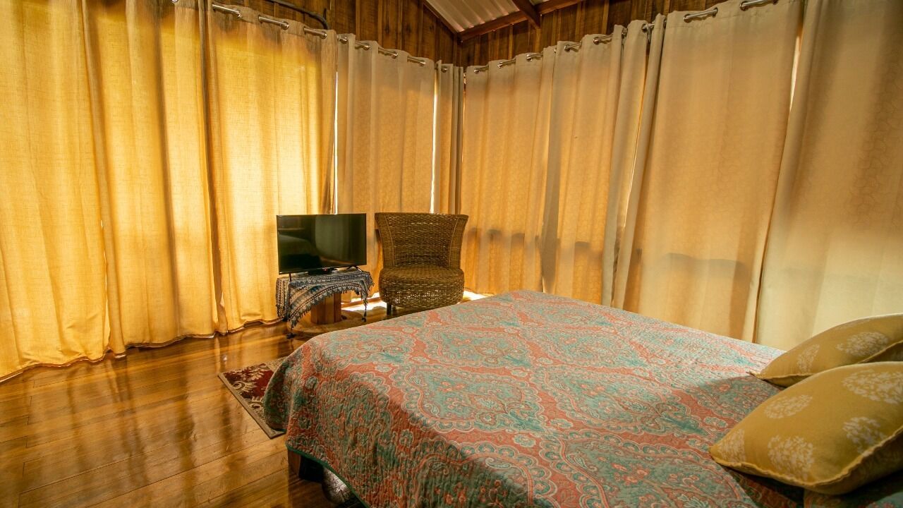 A bedroom with a bed, a chair, a TV, and curtains.