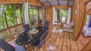Un interior de madera con una mesa de comedor, sillas, un sofá y grandes ventanales que ofrecen vistas a zonas verdes.