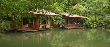 Deux maisons en bois flottantes, dotées de terrasses ouvertes, entourées d’une végétation luxuriante et bordées d’une étendue d’eau calme.