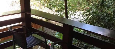 A wooden deck with two wicker chairs and a table, overlooking a lush garden with dense foliage.